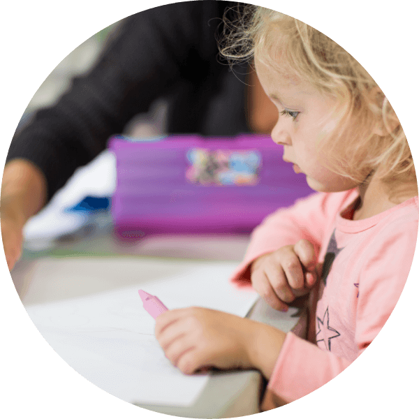 A young child drawing with an adult at a table.