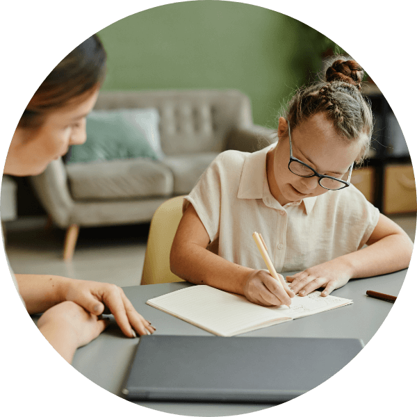 A child writing in a notebook with an adult beside her.