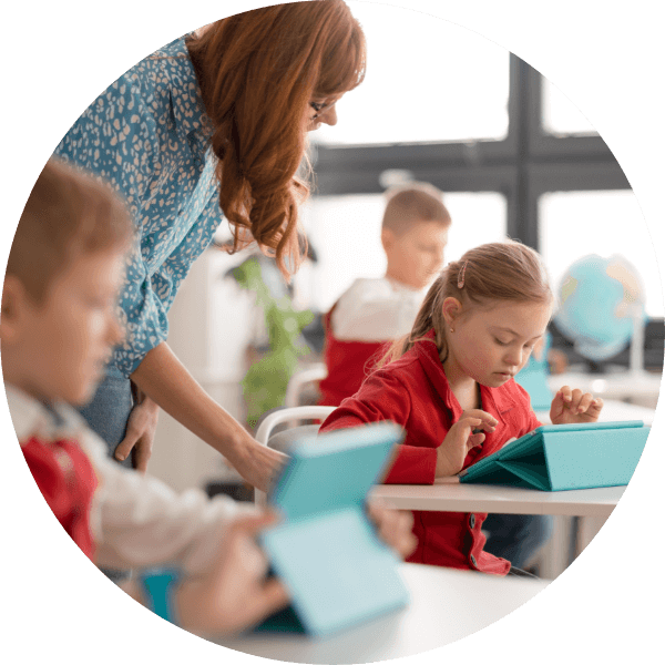 A teacher helping a pupil use a tablet in a classroom.